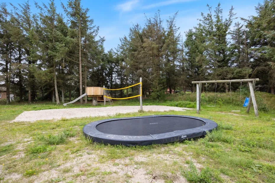 Zona de juegos al aire libre con trampolín redondo, columpios y una red baja.