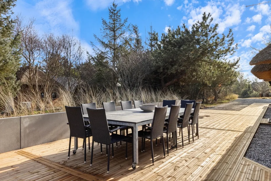 Una zona de comedor al aire libre con una mesa larga y sillas sobre una terraza de madera.