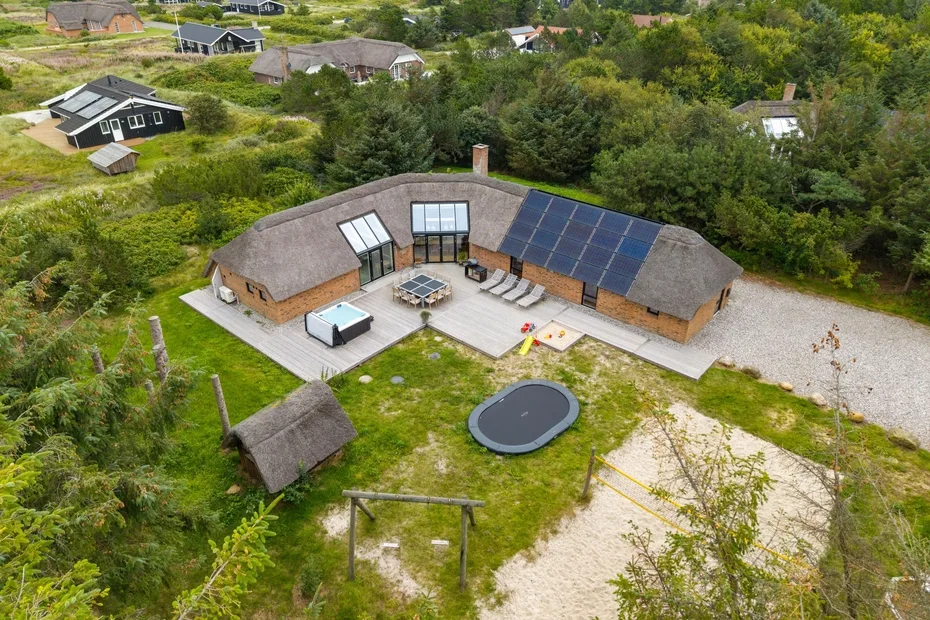 Vista aérea de una casa curva con paneles solares, una terraza y un jardín.