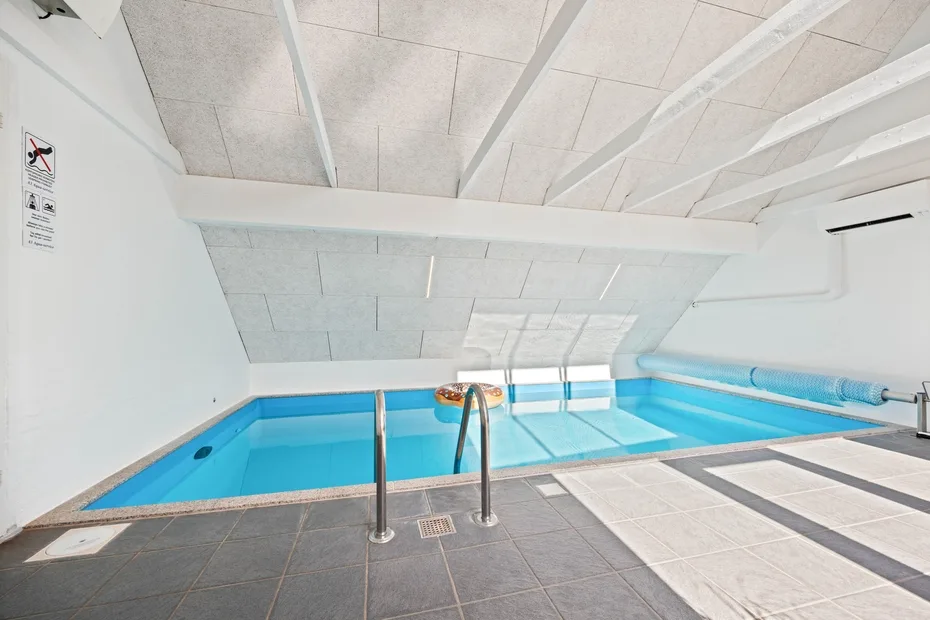 Una piscina cubierta bajo un techo blanco inclinado, con suelo de baldosas.
