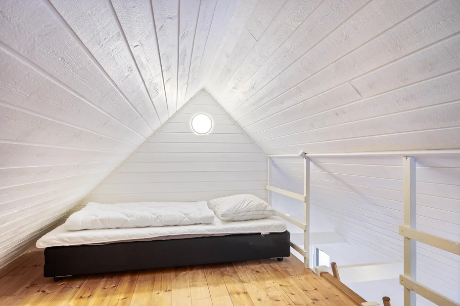 Una cama está bajo un techo inclinado en una pequeña zona para dormir en el ático.