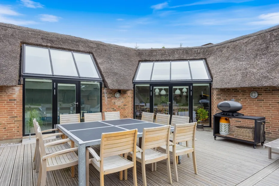 Una zona de comedor al aire libre con una mesa y sillas junto a grandes ventanas.