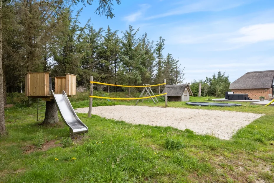 Zona de juegos al aire libre con tobogán, suelo de arena y red de voleibol.