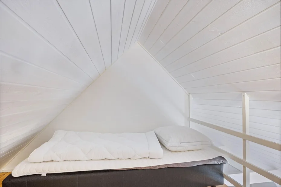 Una cama está bajo un techo blanco inclinado con paneles, en un dormitorio tipo loft.