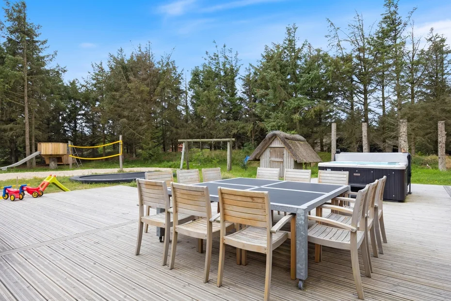 Un patio exterior con una mesa grande y asientos de madera, junto a una zona de juegos.