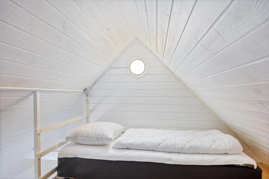 Una pequeña zona para dormir queda bajo un techo blanco inclinado.