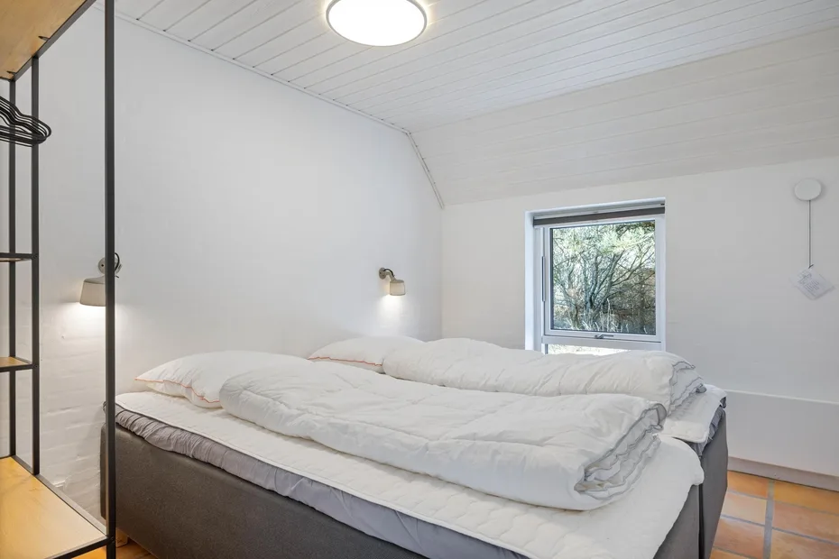 Un dormitorio con una cama bajo un techo inclinado y una ventana.