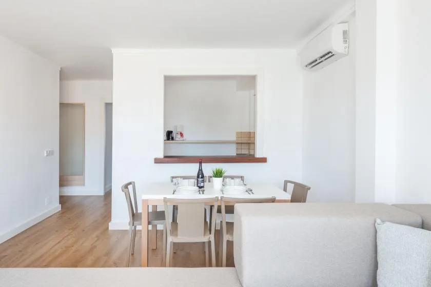 A bright dining area with a table and seating beside a living room.
