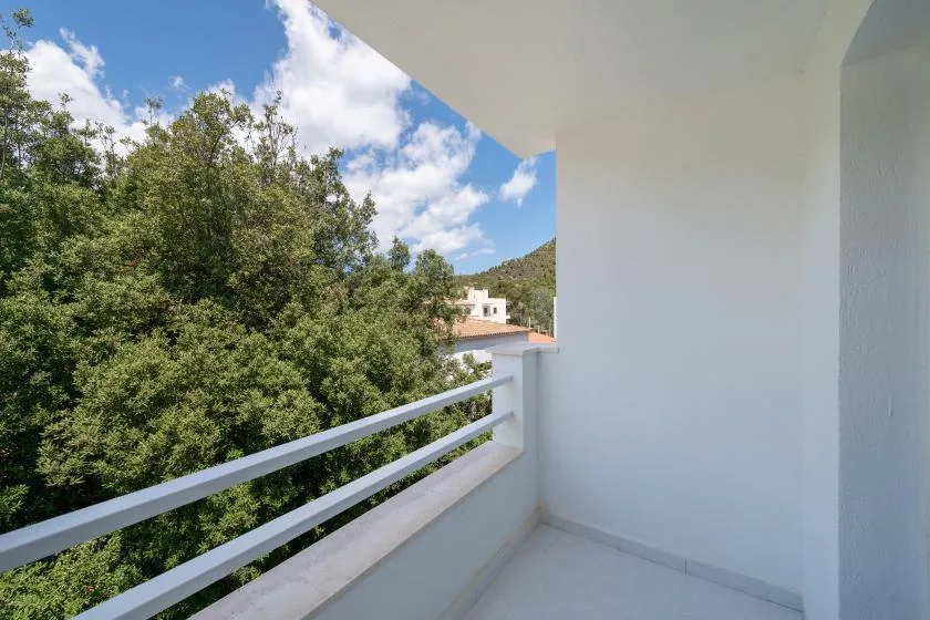 A covered balcony overlooks leafy trees and a distant hillside.