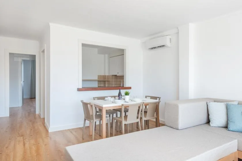 A bright dining area with a table and chairs beside a living room sofa.