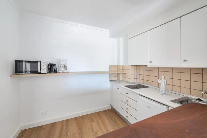 A bright kitchen with white cabinets, a countertop, and wood flooring.