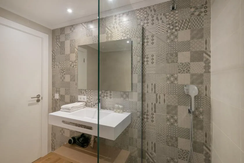 A bathroom with a wall-mounted sink, mirror, and patterned tile.