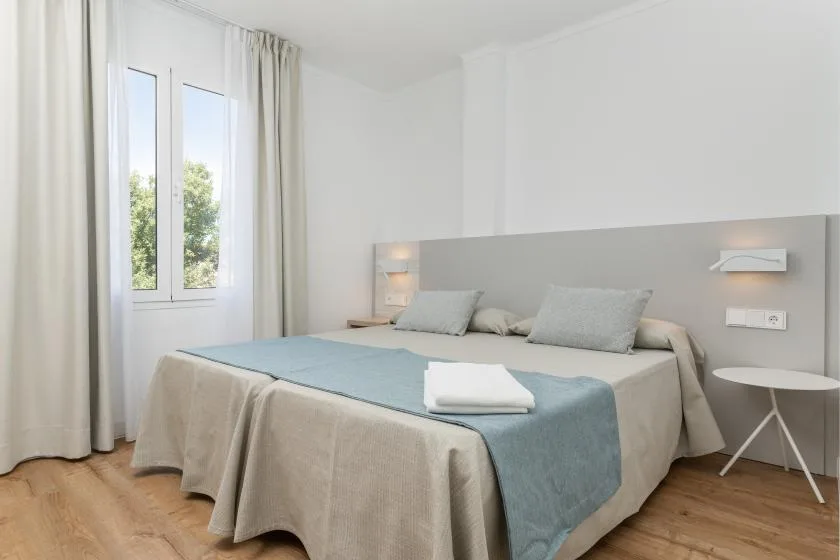 A bright bedroom with a bed and a window overlooking greenery.