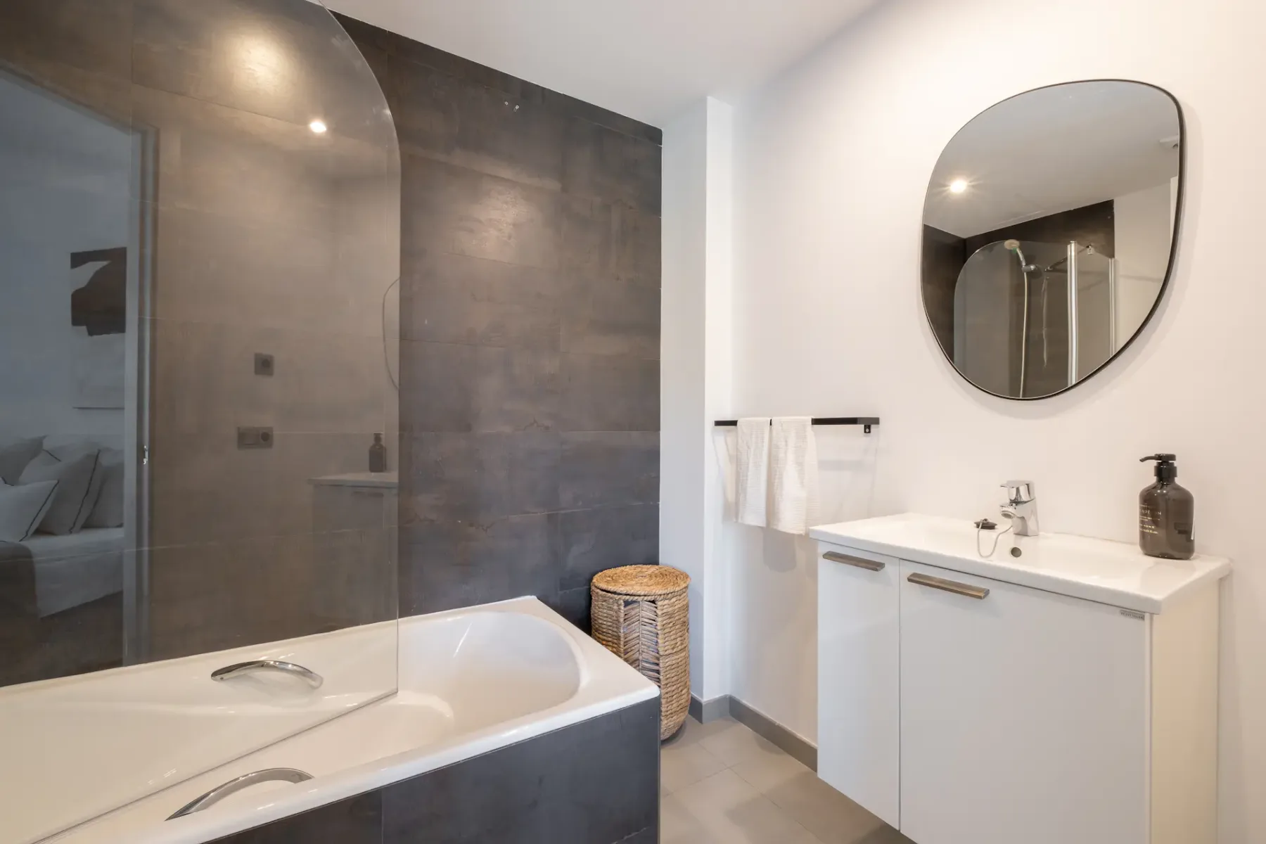 A bathroom with a bathtub, sink, and round wall mirror.