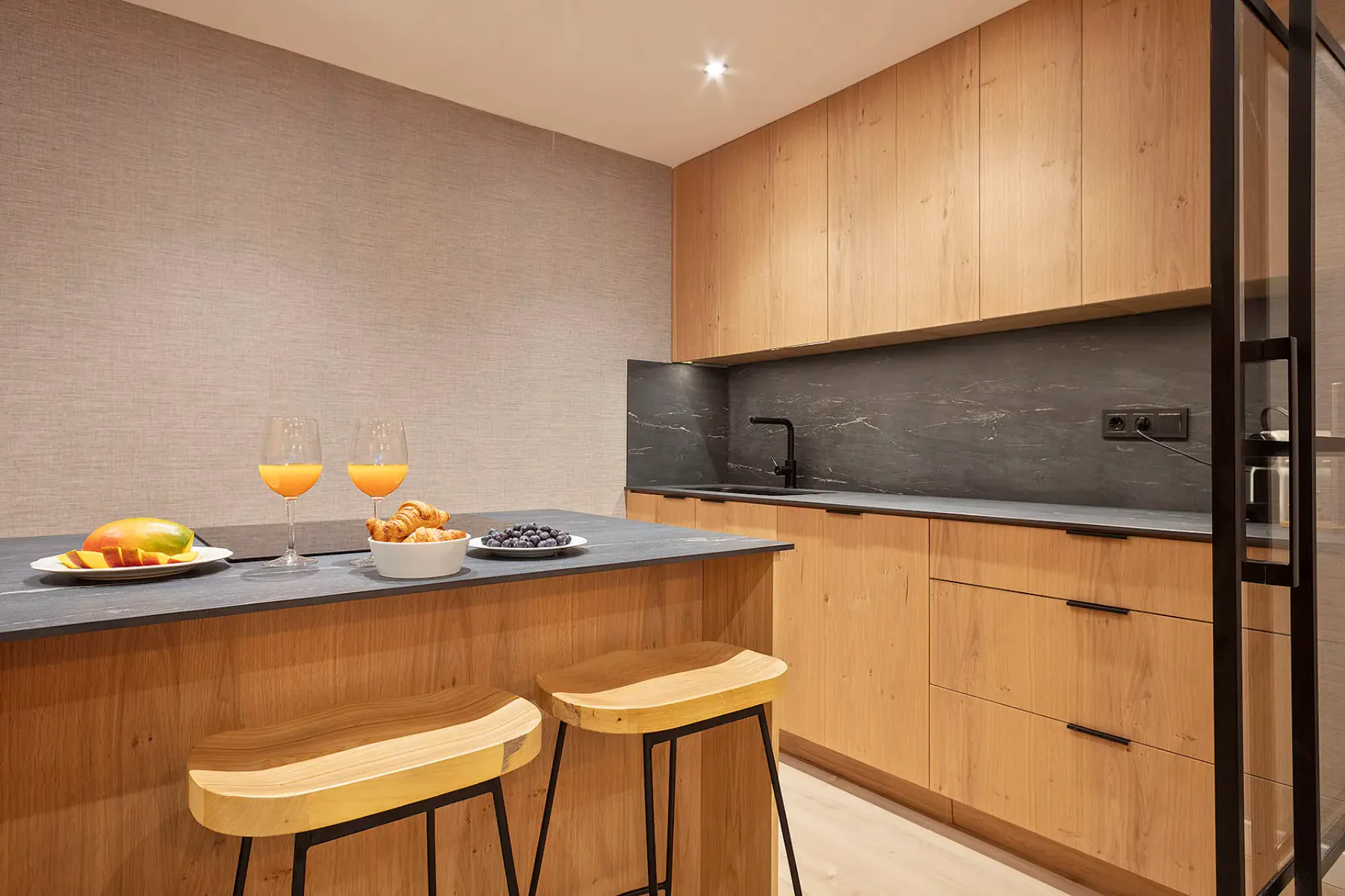 Modern open-concept kitchen and living area with wooden floors and ceiling beams. The kitchen features sleek cabinetry and a large island, while the living room has large windows and cozy seating.