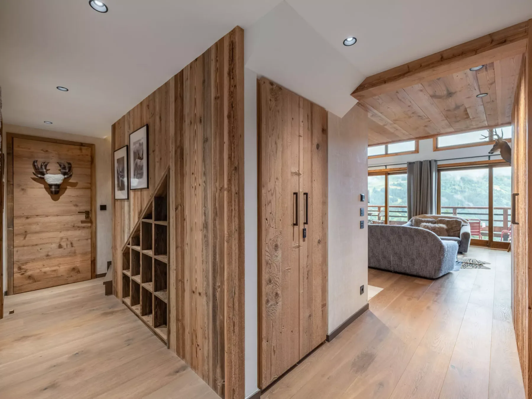 A wood-paneled hallway opens into a living area with seating and large windows.