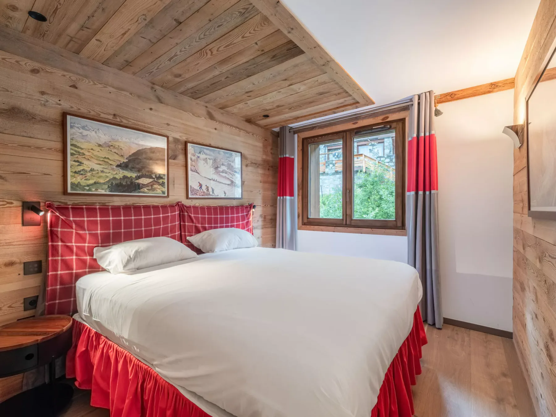A bedroom with a large bed beneath a wood-paneled ceiling and a window.