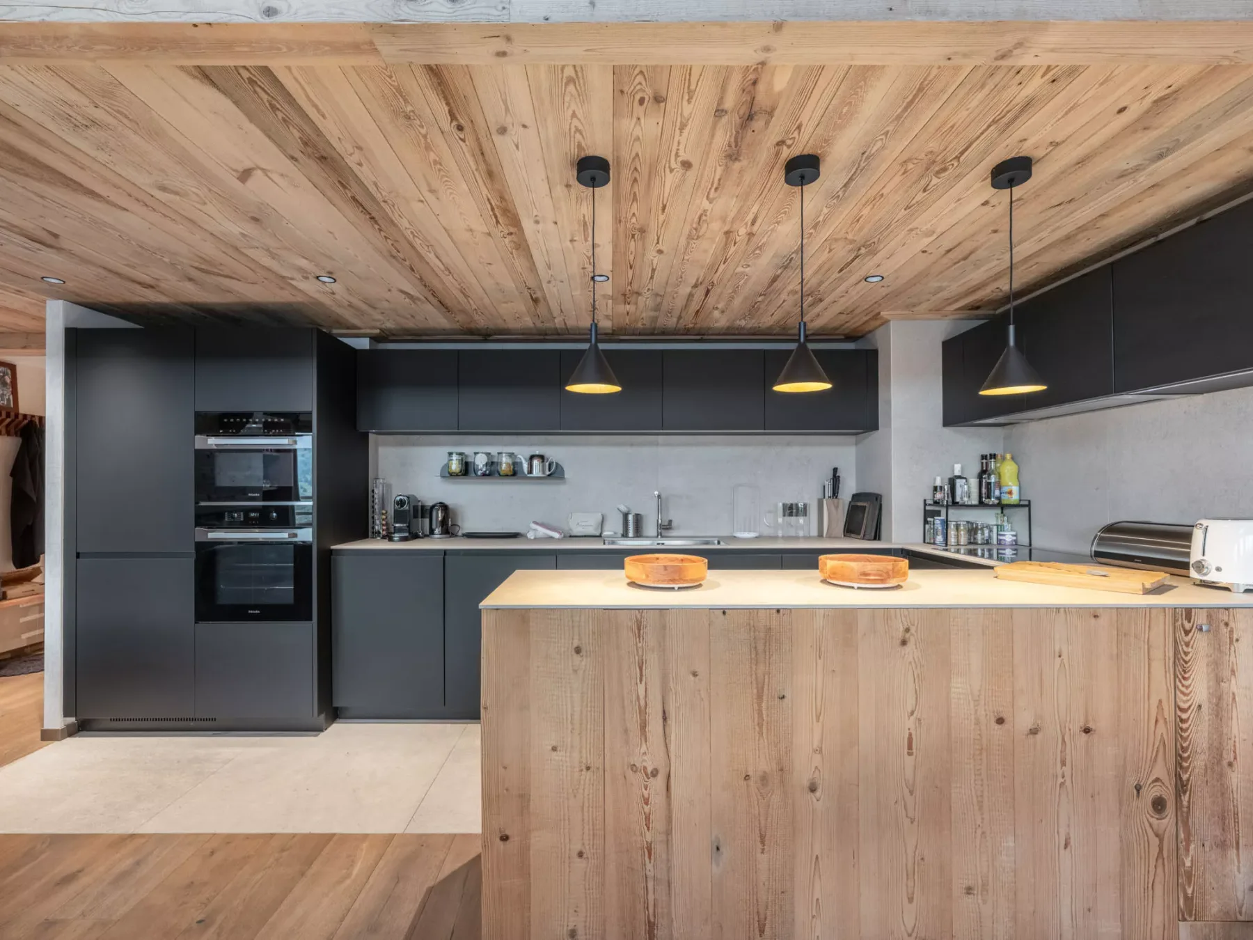 A modern kitchen with dark cabinetry, a wood island, and pendant lights.