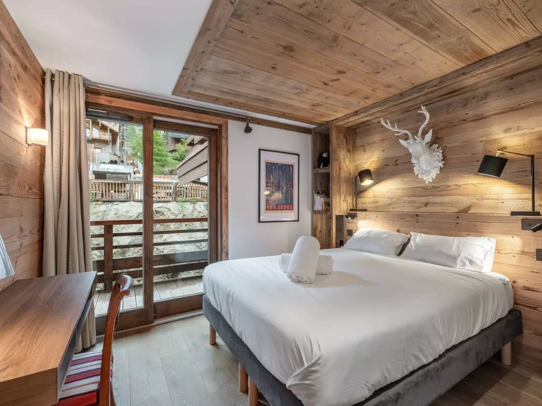 A bedroom with a large bed, wood-paneled walls, and glass doors opening onto a balcony.
