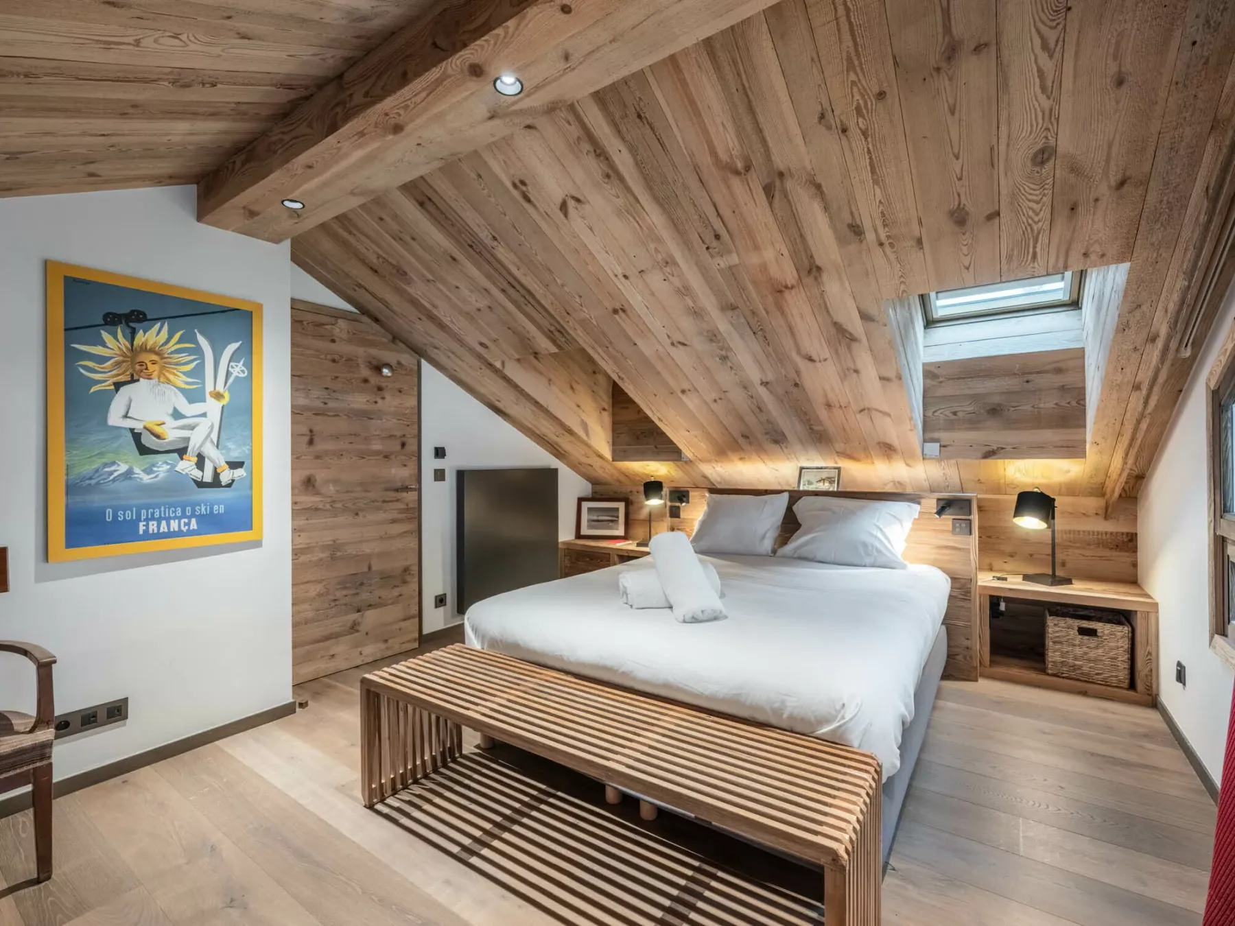 A bedroom with a bed beneath a sloped wood ceiling and a skylight.