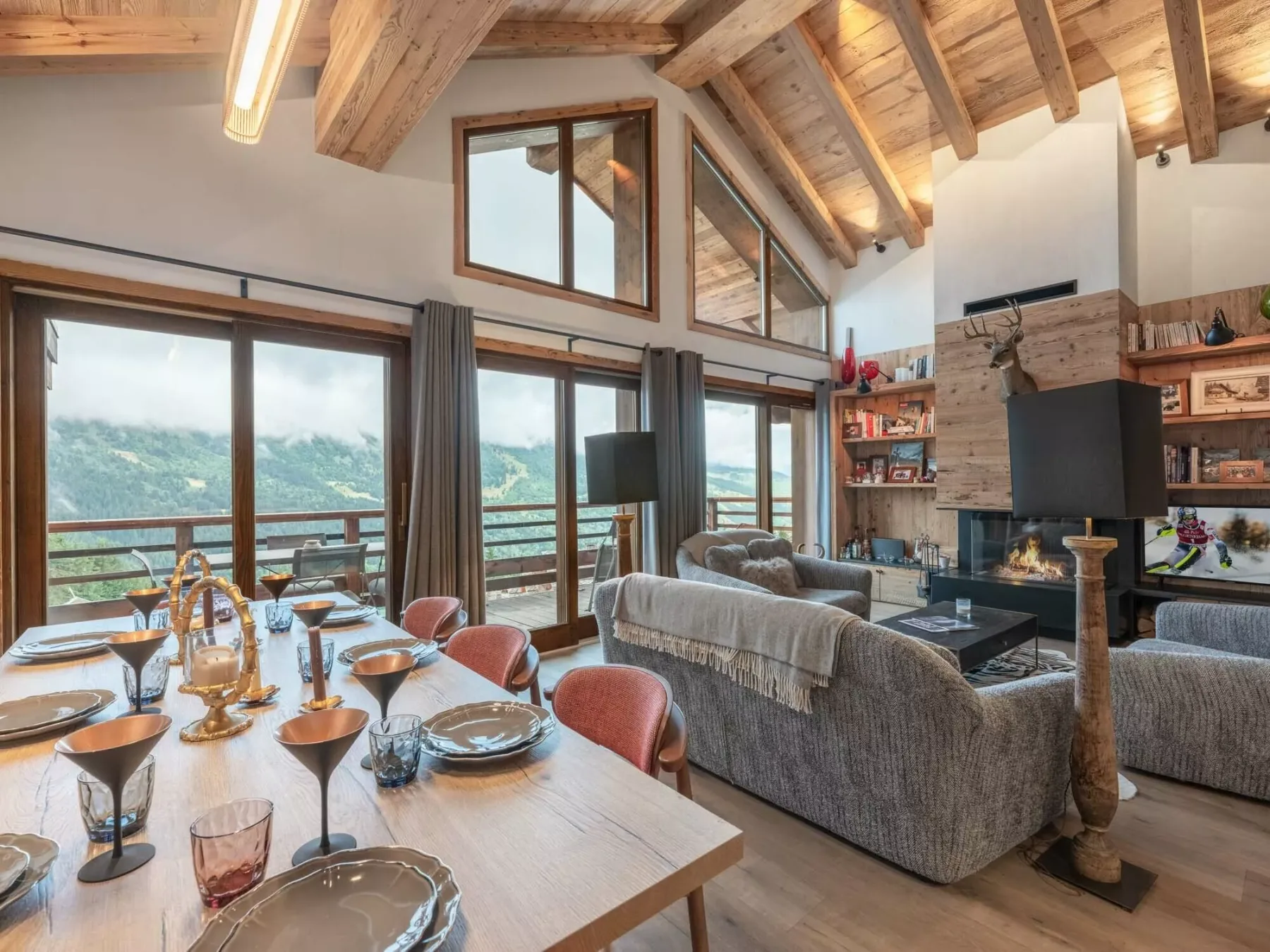 A dining and living area with large windows overlooking a green mountain landscape.