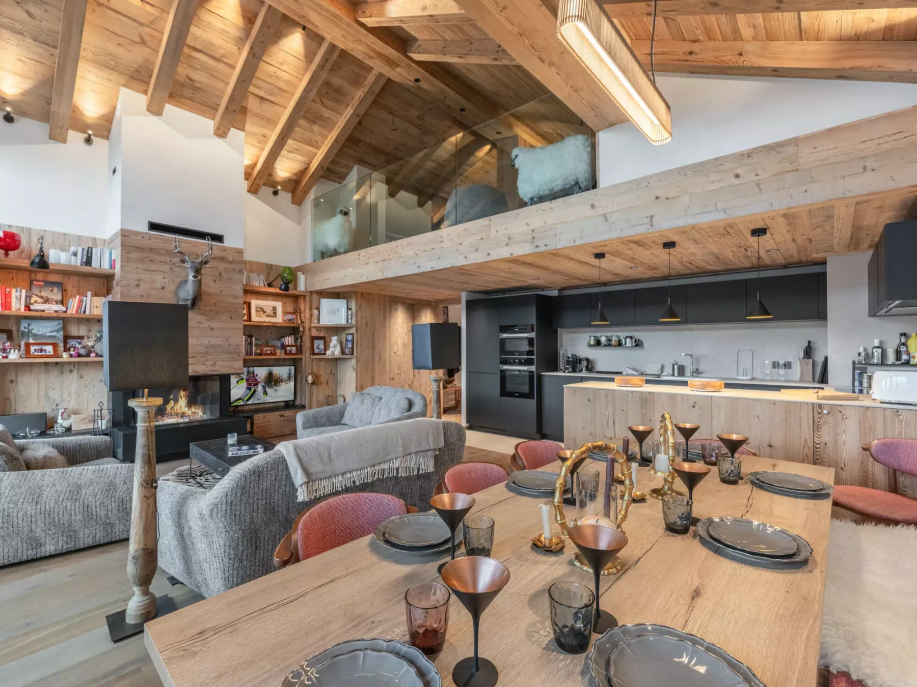 A dining and living area features a long wooden table and an open kitchen.
