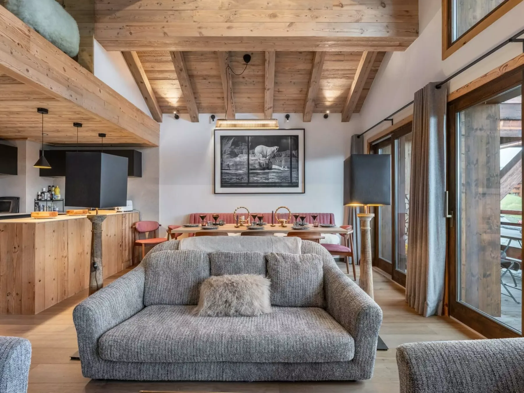 A living room with a gray sofa, dining table, and exposed timber ceiling.