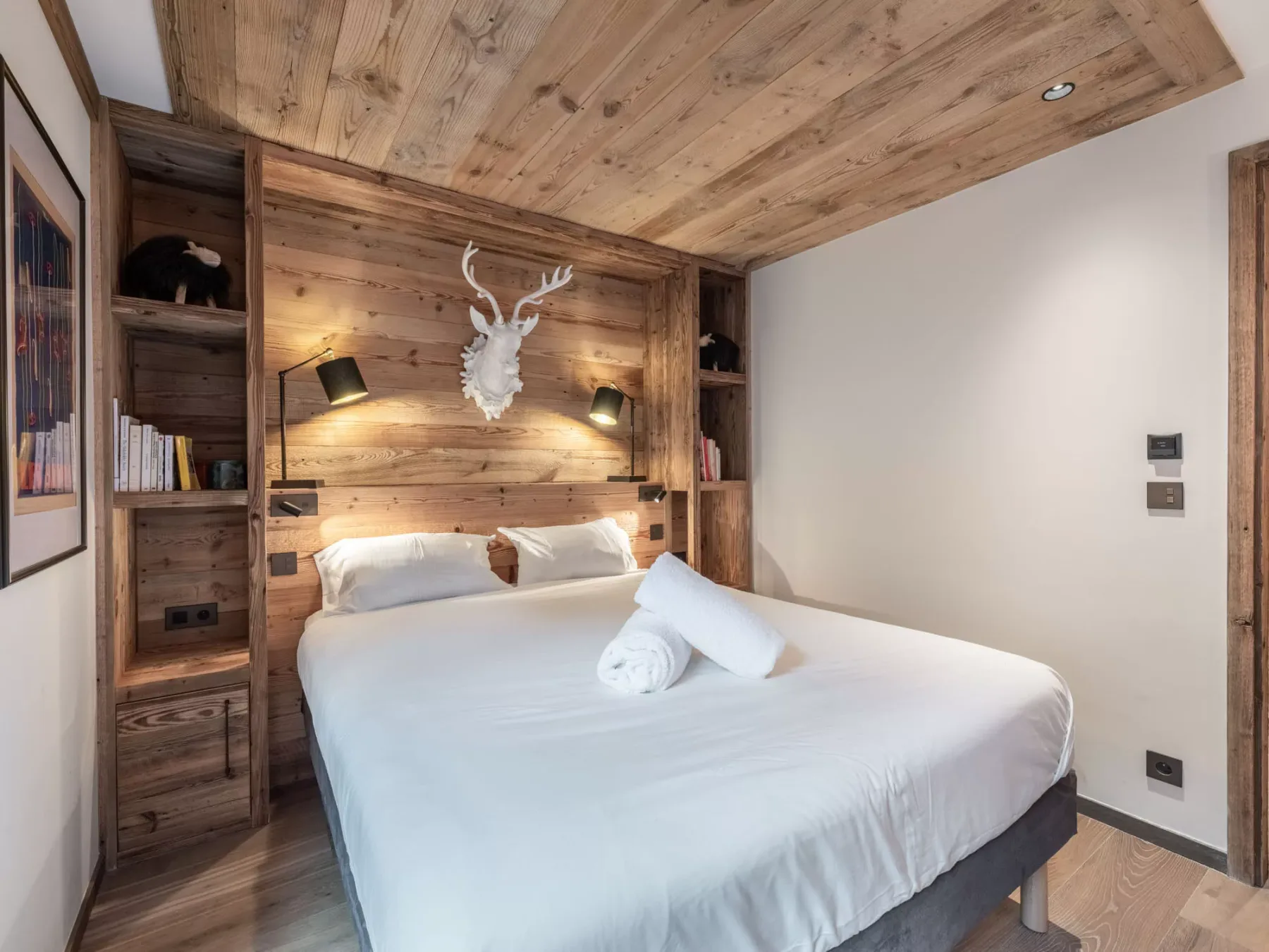 A bedroom with a neatly made bed beneath a wood-paneled ceiling.