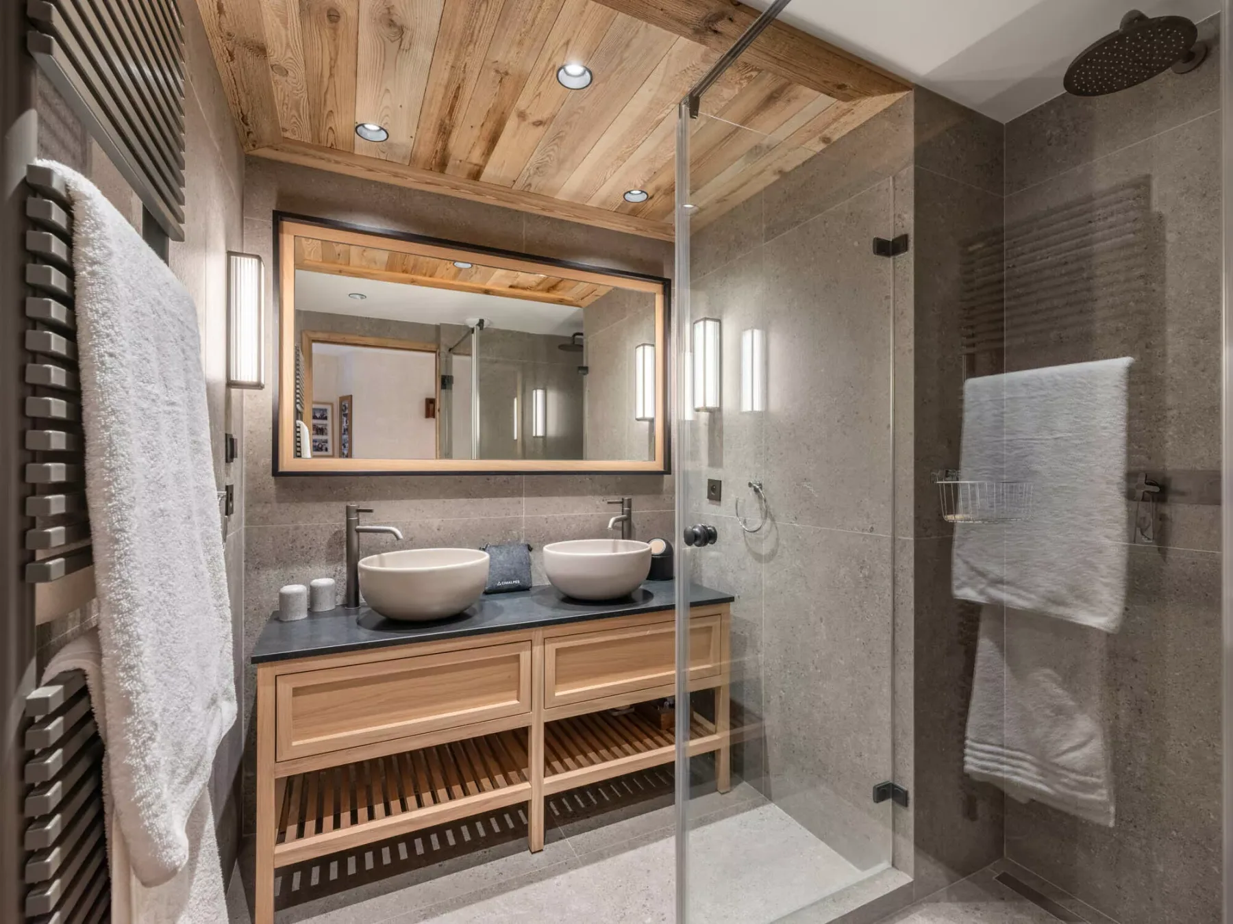 A bathroom with a wood vanity, wide mirror, and glass shower.