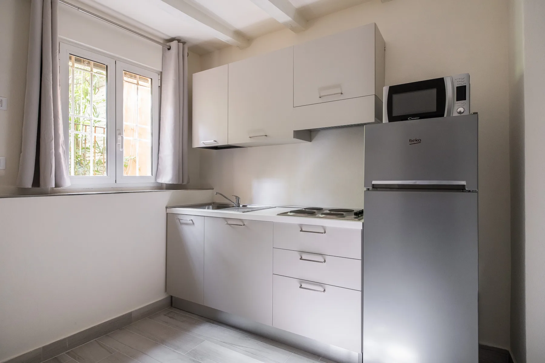 Una cocina pequeña con gabinetes blancos, un refrigerador y una ventana.