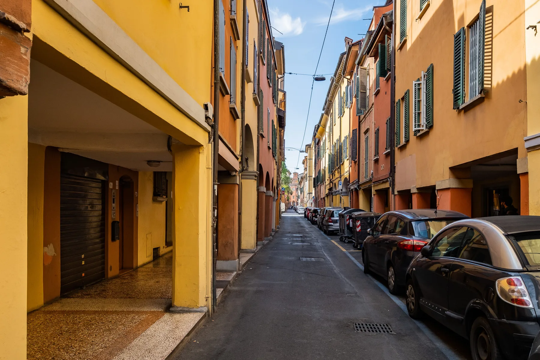 A narrow street runs between colorful buildings, with parked cars along the sides.