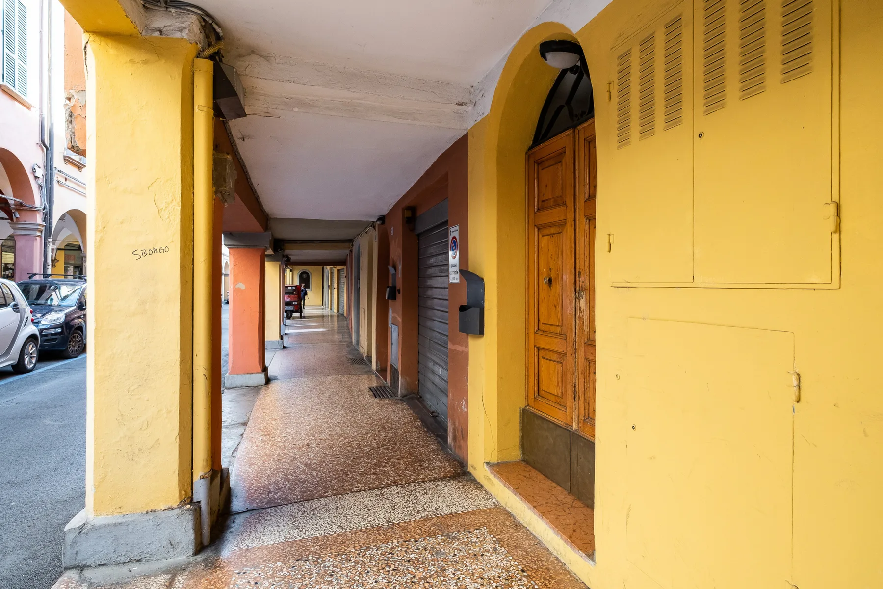 A covered building passage with yellow walls and a wooden doorway.