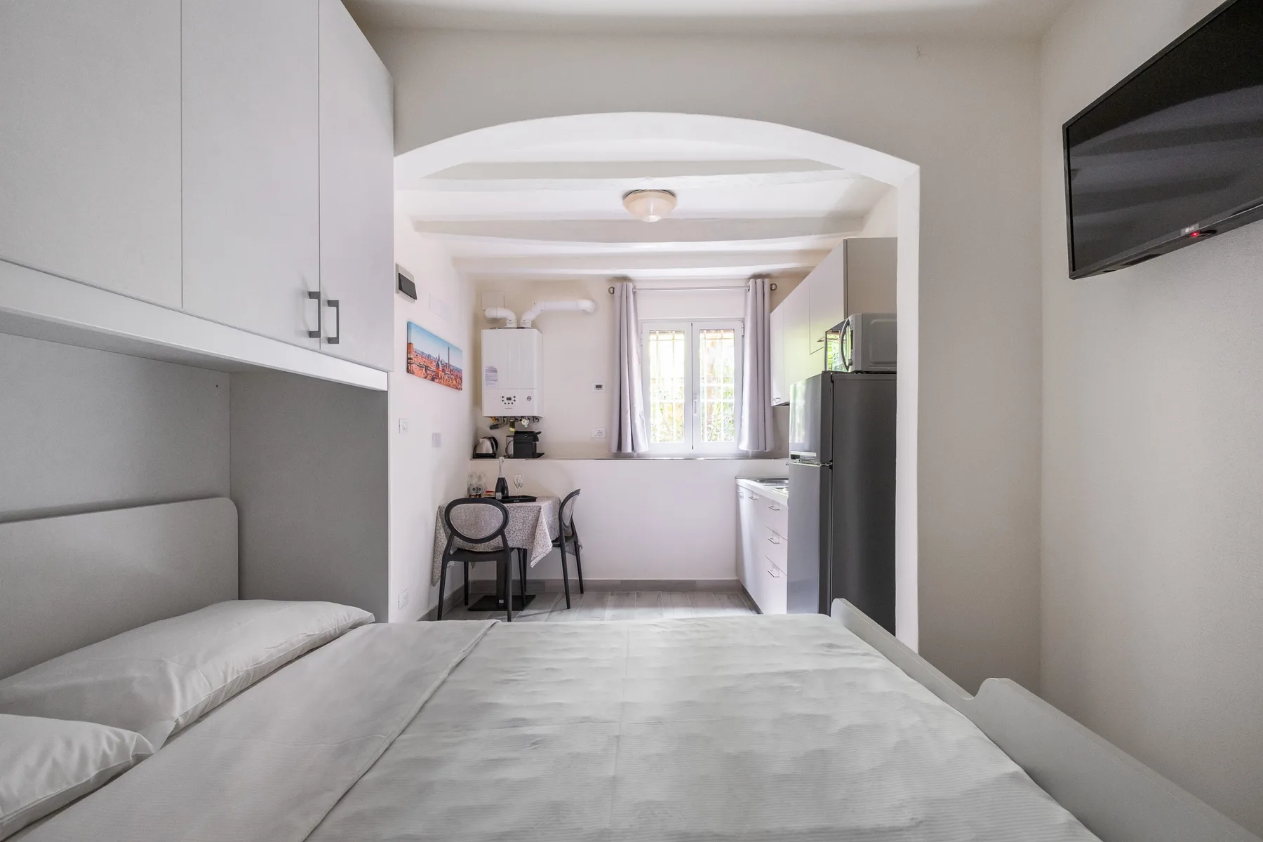 A bedroom with a bed, built-in cabinets, and a small dining area by the window.
