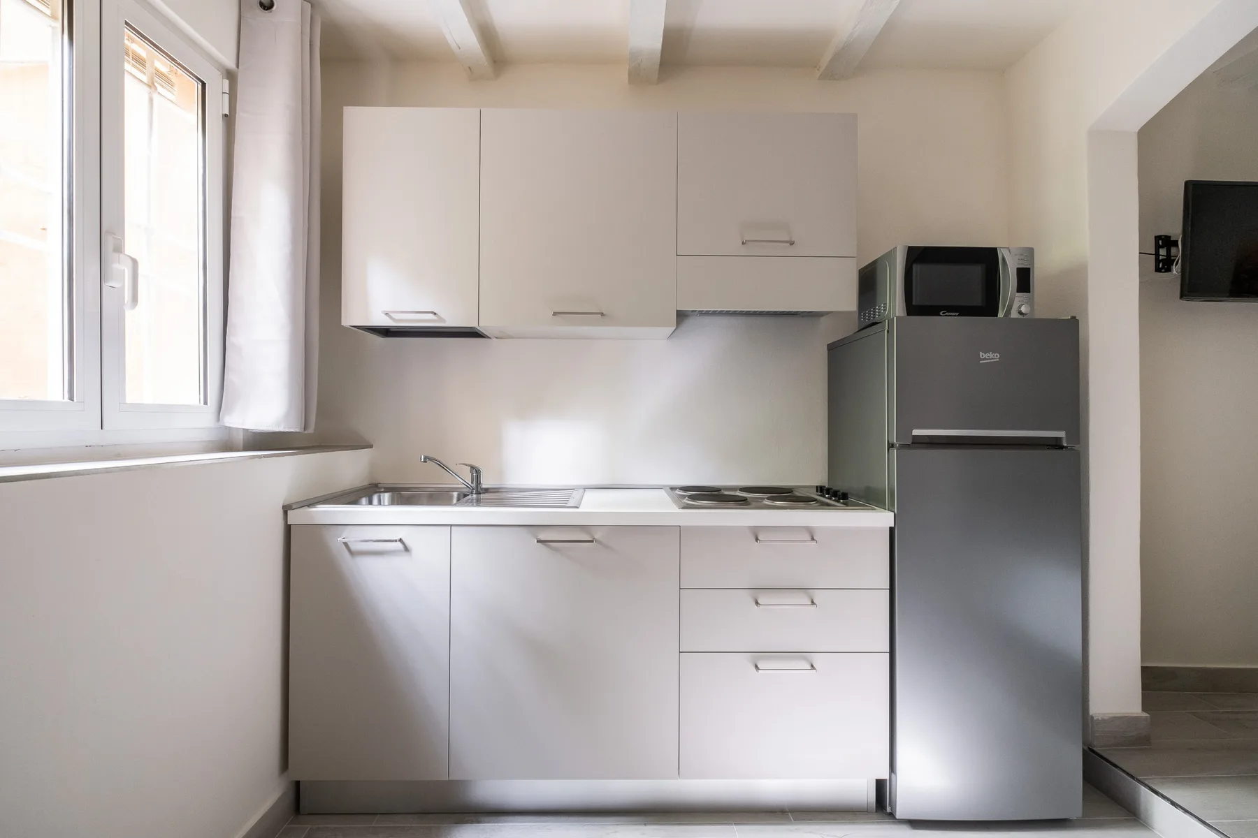 A compact kitchen with white cabinets, a countertop, and a refrigerator.