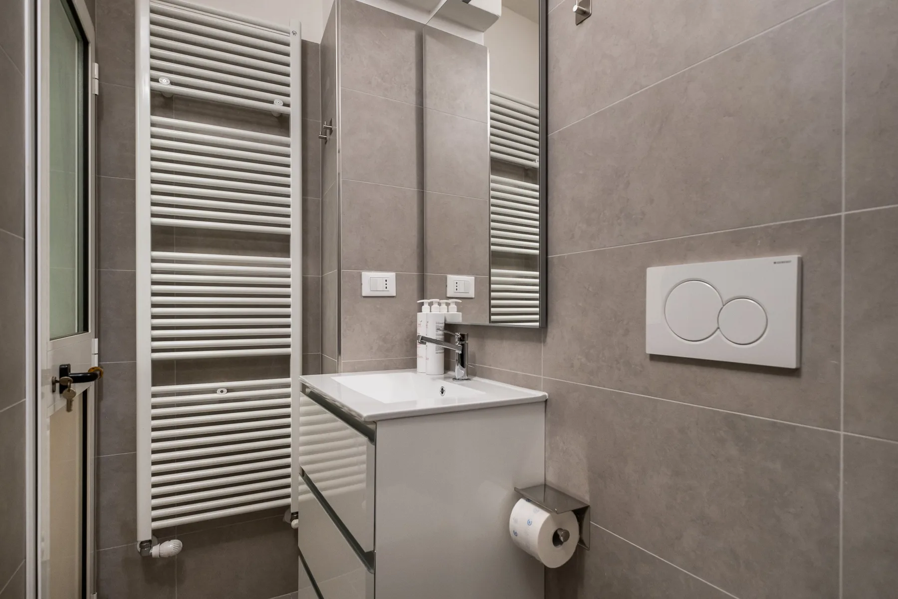A tiled bathroom with a vanity, wall mirror, and towel radiator.