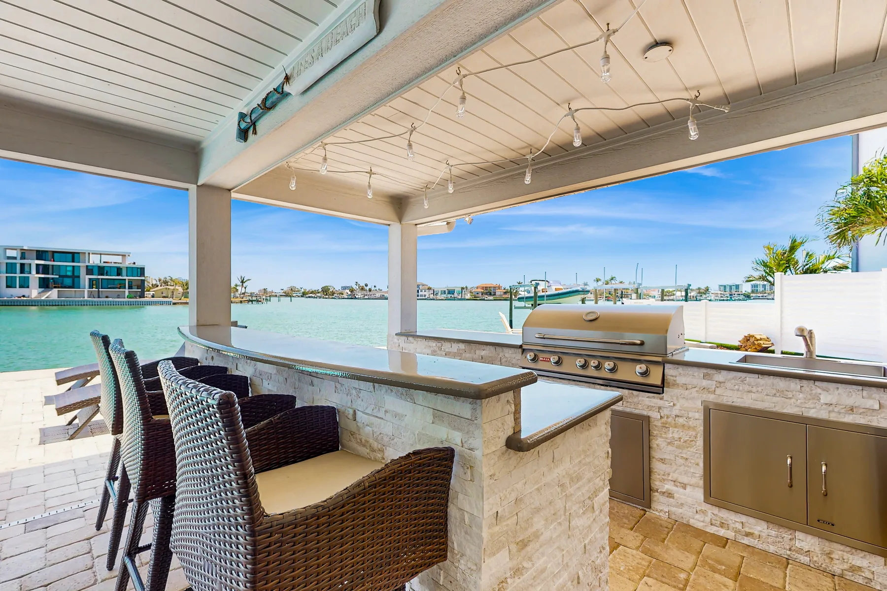 A covered outdoor kitchen and counter overlook the water, with seating nearby.
