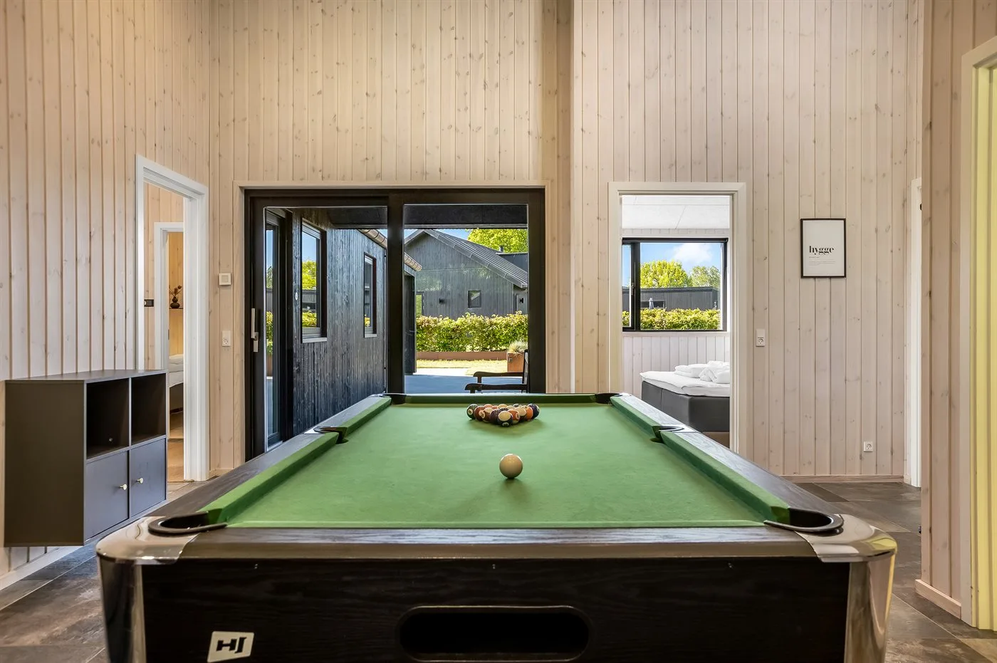 Una mesa de billar está en una habitación luminosa con grandes puertas de vidrio.