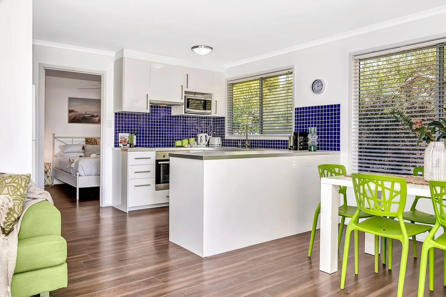 Una cocina luminosa con isla blanca y asientos verdes en el comedor.