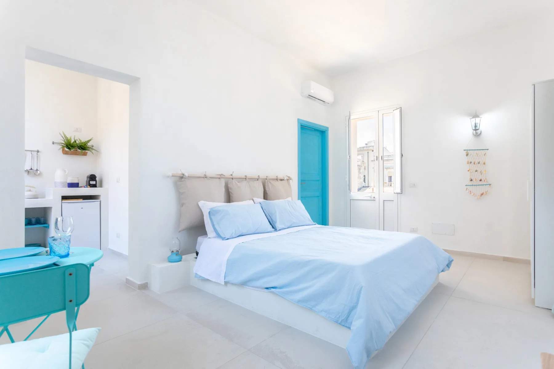 Un dormitorio luminoso tiene una cama con ropa de cama azul claro junto a una puerta turquesa.