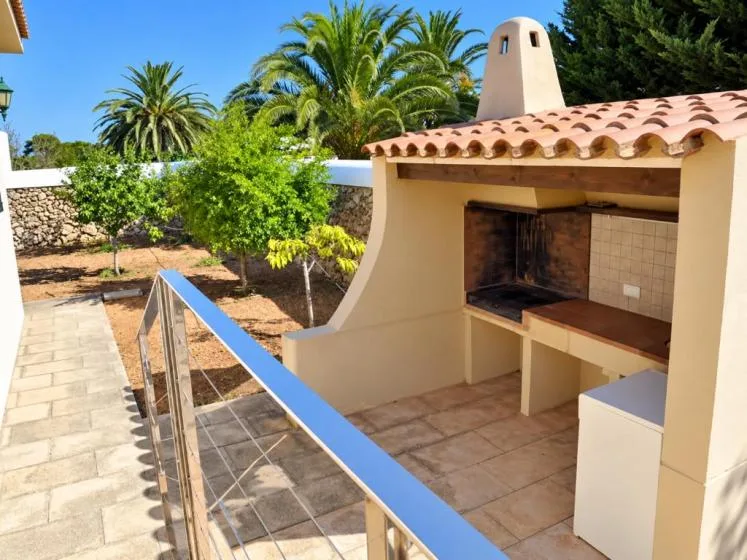 Una zona de barbacoa al aire libre con encimera de azulejos y vegetación.