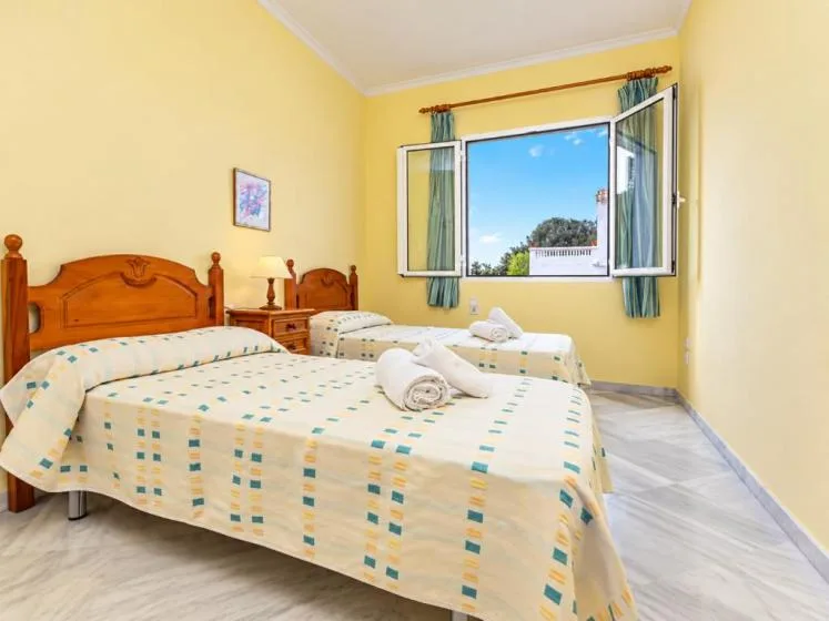 Un dormitorio amarillo con dos camas y una ventana abierta con vista al cielo.