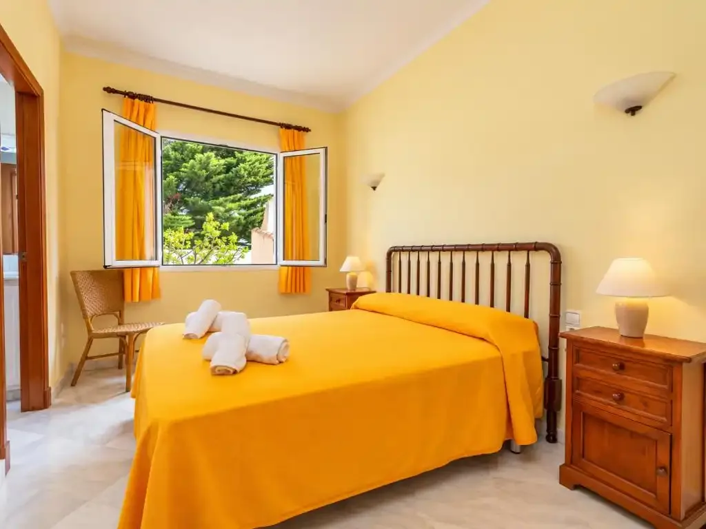 Un dormitorio con una colcha amarilla y una ventana abierta.