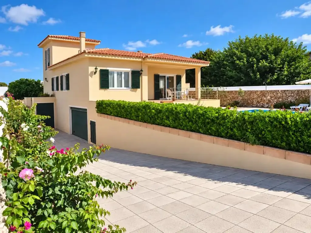 Una casa de color crema con patio embaldosado y jardín frondoso.
