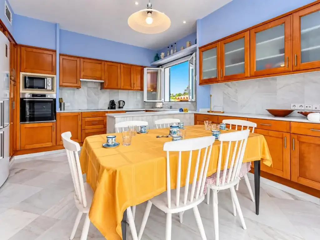 Cocina y comedor luminosos con armarios de madera y una mesa preparada para comer.
