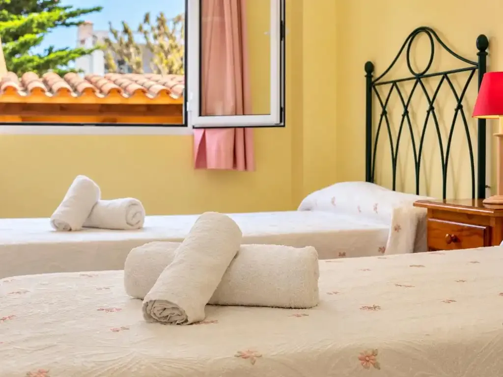 Un dormitorio con ropa de cama clara y toallas dobladas.