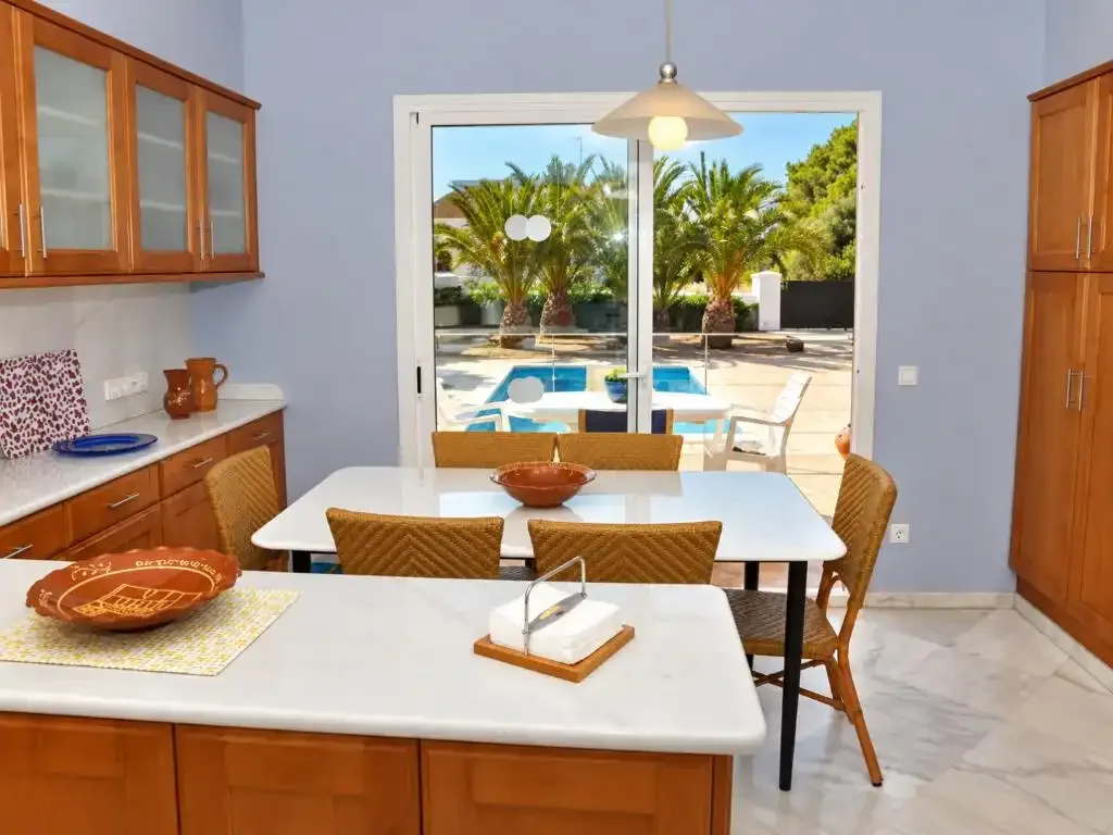 Un comedor con mesa y encimera de cocina da a un patio junto a la piscina.