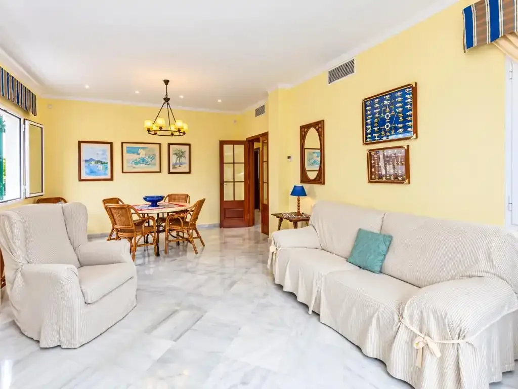 Una sala luminosa con asientos claros y un comedor.