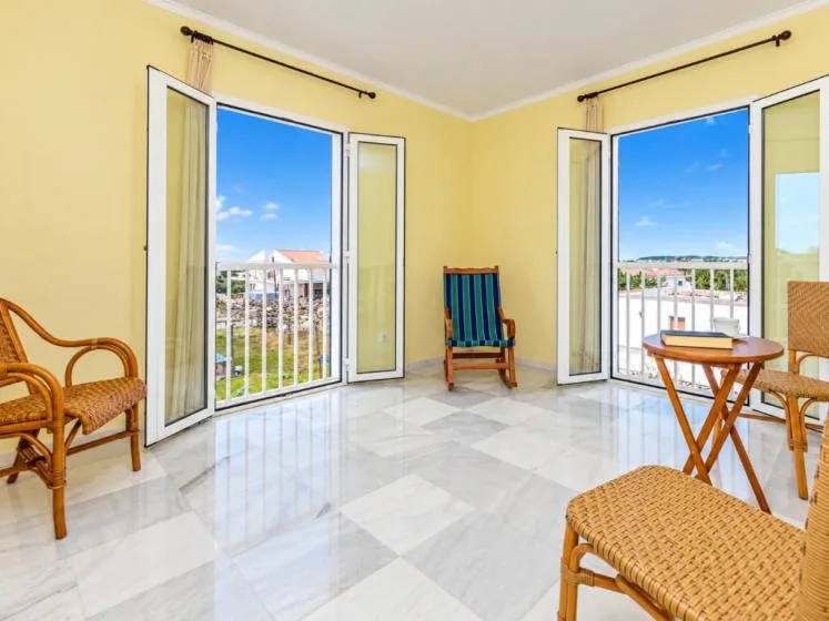 Una sala luminosa con puertas abiertas al balcón, asientos de mimbre y vistas al exterior.
