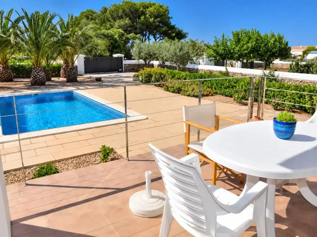 Un patio con asientos al aire libre da a una piscina y un jardín ajardinado.