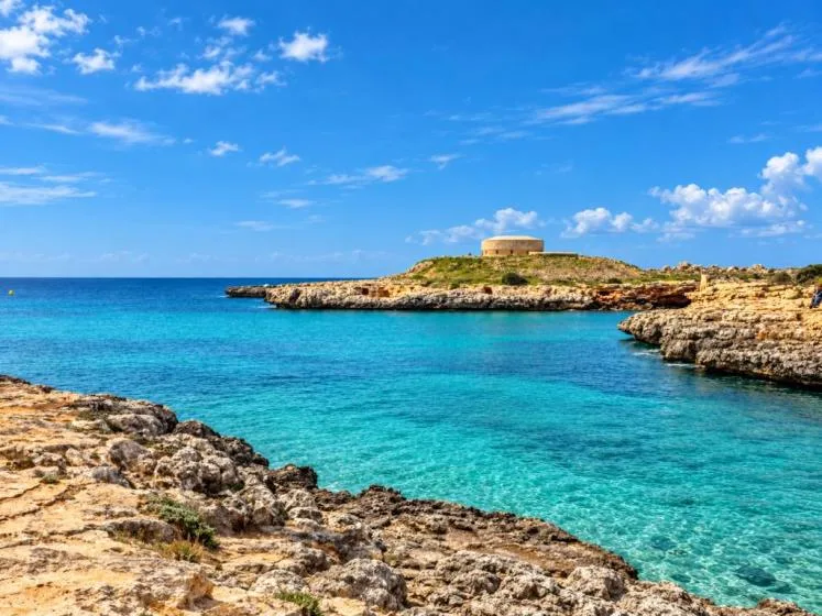 Una bahía de aguas turquesas está rodeada de orillas rocosas bajo un cielo azul.